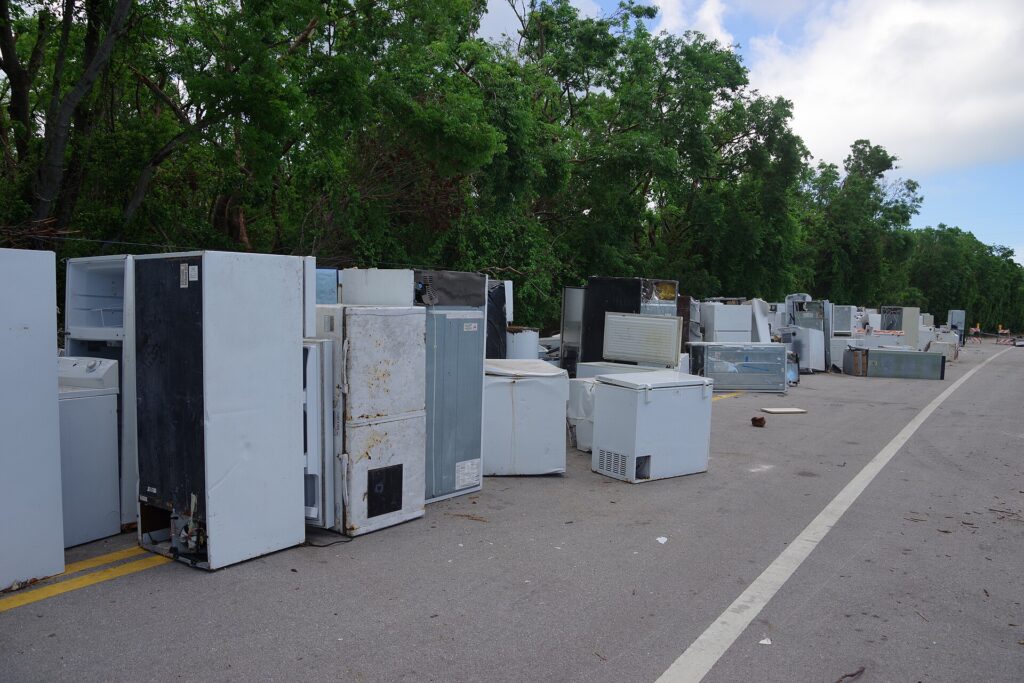 A row of old refrigerators, upright freezers and chest freezers lined up outdoors for recycling